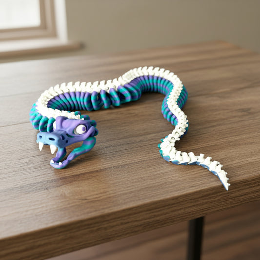 A 3D printed skeleton snake with flexible movement, featuring a moveable jaw, protruding teeth and cartoon-esque eyes. Laying on a wooden table. 