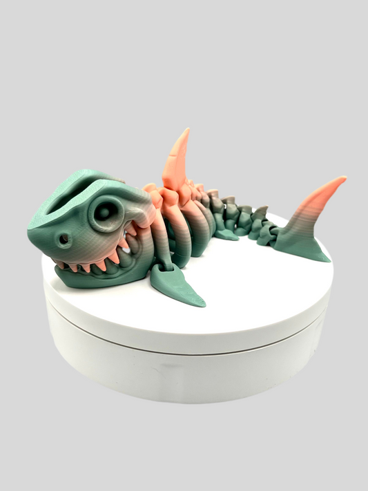 A small sized 3D printed khaki and coral coloured skeleton shark figurine with detailed features and wide mouth, showing teeth. Positioned on a white display base