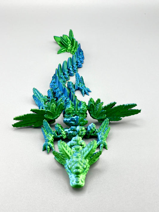 A 3D printed winged dragon in shiny green and blue colouring, with outstretched wings and an axolotl's head. Set on a light grey background. 