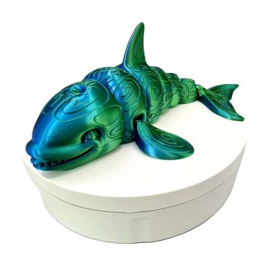 A 3D-printed orca with a tattooed all-over print, detailed facial features and exposed teeth. Positioned laying down on a white base.