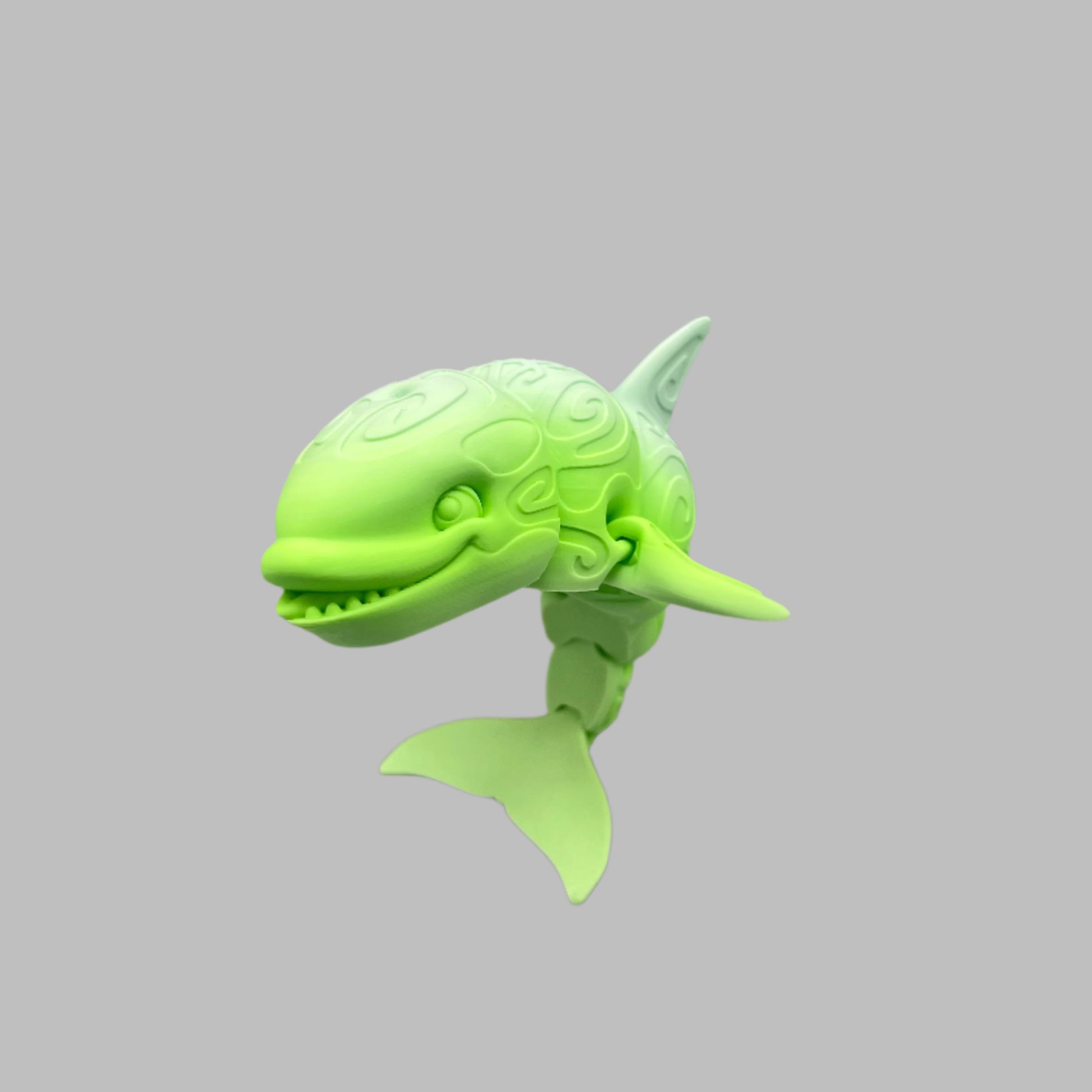 A 3D-printed orca with a tattooed all-over print, detailed facial features, including a smile, exposed teeth and tongue. Positioned standing up on it's tail. Set against a light grey background
