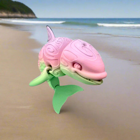 A 3D-printed orca with a tattooed all-over print, detailed facial features, including a smile and exposed teeth and tongue. Positioned standing on it's tail on the beach.