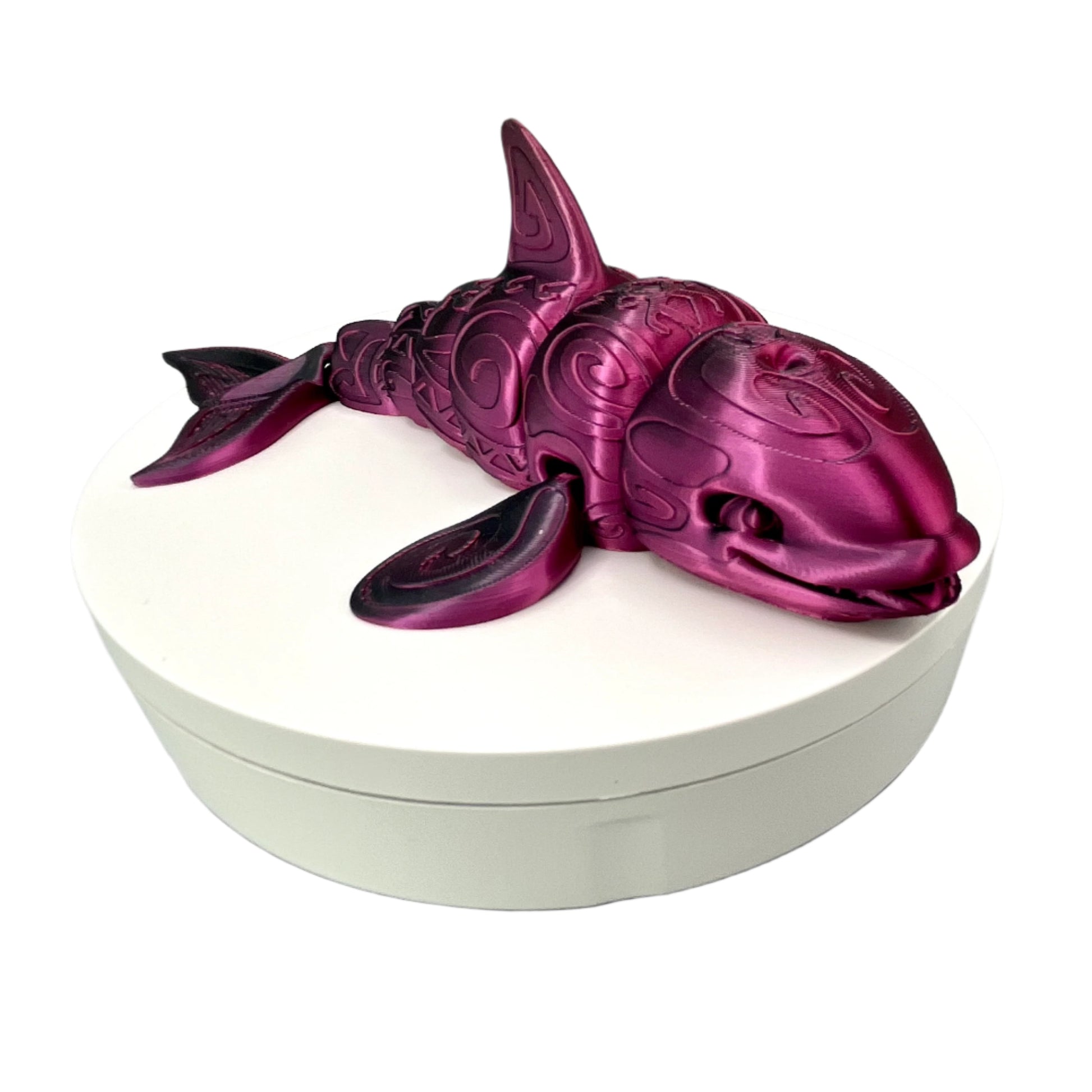 A 3D-printed orca with a tattooed all-over print, detailed facial features, including a smile, exposed teeth and tongue. Positioned laying down on a white base.