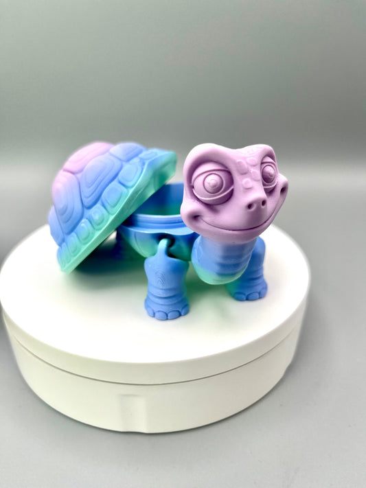 A 3D-printed trinket box in the shape of a tortoise with a detachable shell and cute expressive face, displayed on a white platform.